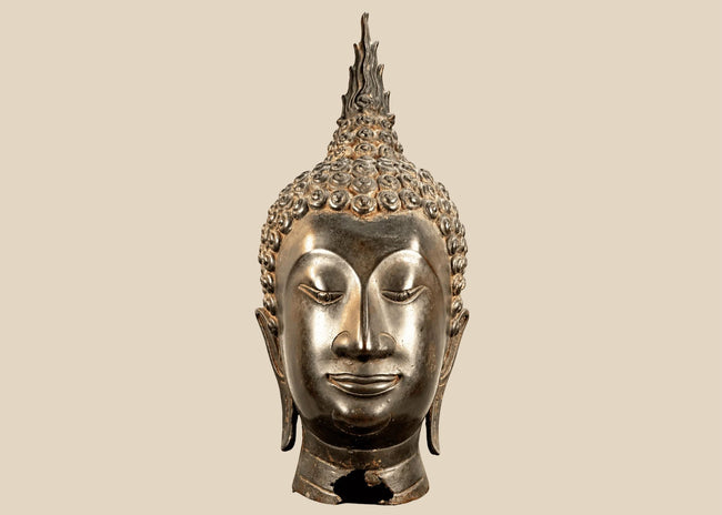 Large Thai Buddha head in Sukhothai style with serene facial features, spiral hair curls, and a tall flame-shaped finial.