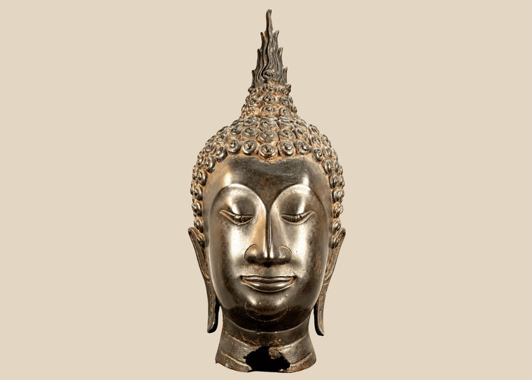 Large Thai Buddha head in Sukhothai style with serene facial features, spiral hair curls, and a tall flame-shaped finial.