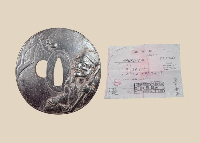 Antique Japanese iron tsuba with mixed-metal sage and spider design displayed beside its Japanese purchase receipt