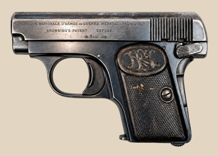 Deactivated FN Browning Model 1906 pocket pistol with checkered grips and worn blued steel against a beige background.