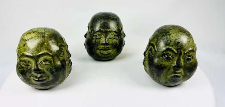 Set of three cast metal Buddhist heads with green patina in traditional brocade box