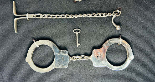 Close-up of antique 19th–20th century iron handcuffs and wrist restraints with original keys, displayed on a dark fabric background.