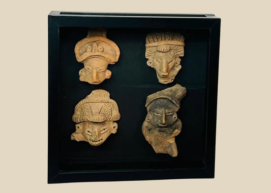 Group of four Pre-Columbian terracotta mask or face fragments, mounted together in a black display frame against a white background, showing varied expressions and headdresses.