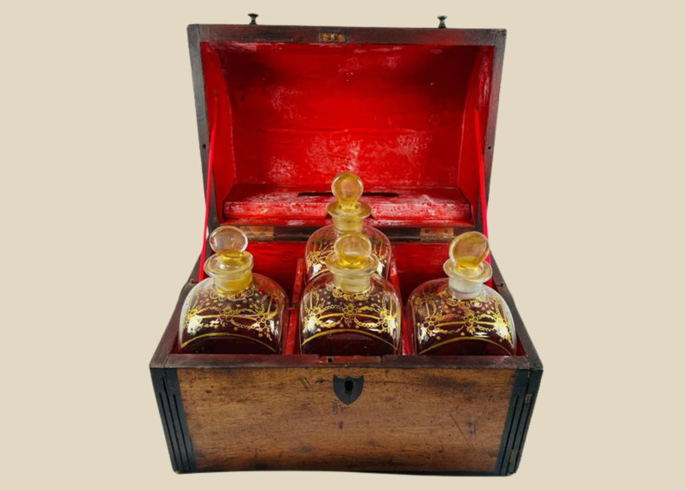 Georgian-era wooden tantalus box with red-painted interior, containing four gilded glass decanters with stoppers, used for securely storing and displaying spirits, early 19th century.