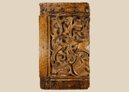 Front view of 16th-century Gothic carved oak panel showing central heraldic shield framed by foliate scrollwork.
