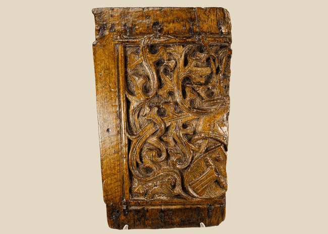Front view of 16th-century Gothic carved oak panel showing central heraldic shield framed by foliate scrollwork.