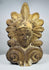 Antique Greek terracotta roof ornament featuring a classical face framed by decorative volutes and a radiating palmette motif.
