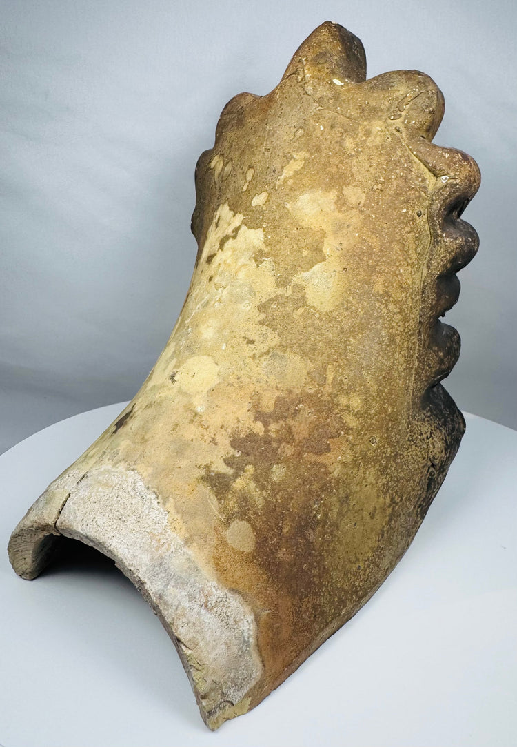 Decorative terracotta antefix from Greece featuring an idealized human face, scrolling volutes, and traditional architectural ceramic construction.