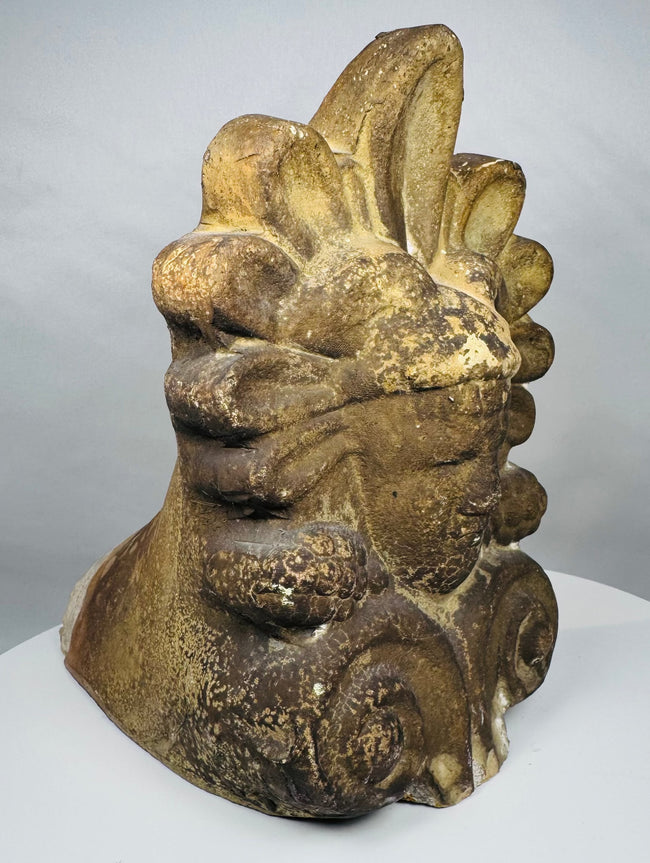 Architectural terracotta ornament from Greece depicting a serene classical face surrounded by traditional decorative motifs and patina.
