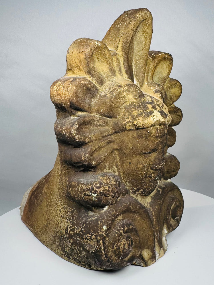 Architectural terracotta ornament from Greece depicting a serene classical face surrounded by traditional decorative motifs and patina.