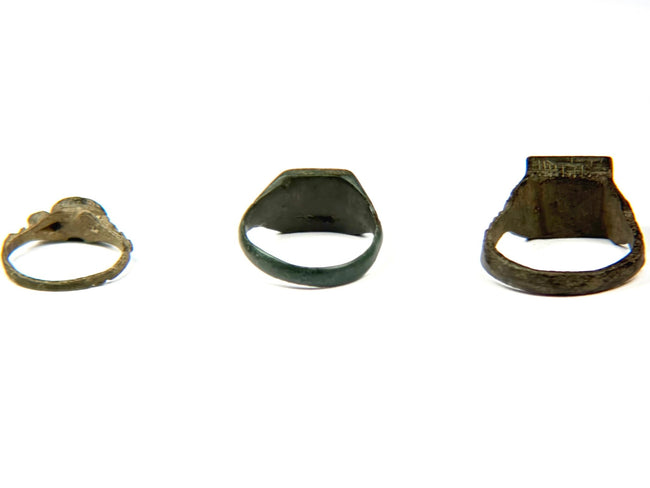 Three Late Roman to Early Byzantine bronze finger rings shown from the back, highlighting their varied bezel shapes, aged patina, and surviving ancient metalwork, circa 3rd–7th century CE.