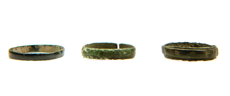 Three ancient bronze finger bands shown in side profile with varied widths, patina and archaeological surface wear