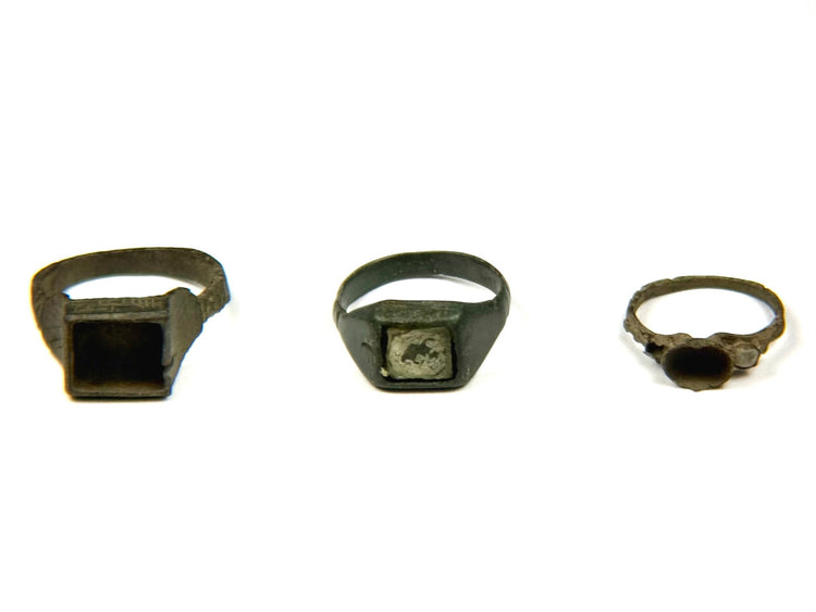 Three Late Roman to Early Byzantine bronze finger rings displayed side by side, featuring square bezel, inset signet and round bezel designs, circa 3rd–7th century CE