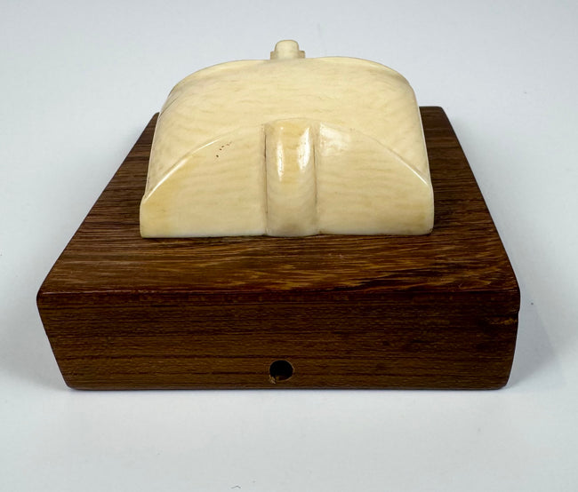 Stylized bone face sculpture with minimalist features and creamy ivory coloration, displayed on an original hardwood mounting board.
