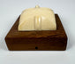 Stylized bone face sculpture with minimalist features and creamy ivory coloration, displayed on an original hardwood mounting board.