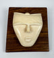 Decorative bone spirit head carving with geometric contours and smooth polished finish, mounted against a rich hardwood display plaque.