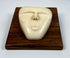 Vintage bone relief carving of a human spirit face with closed eyes and triangular form, mounted on a polished wooden plaque.