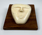 Vintage bone relief carving of a human spirit face with closed eyes and triangular form, mounted on a polished wooden plaque.