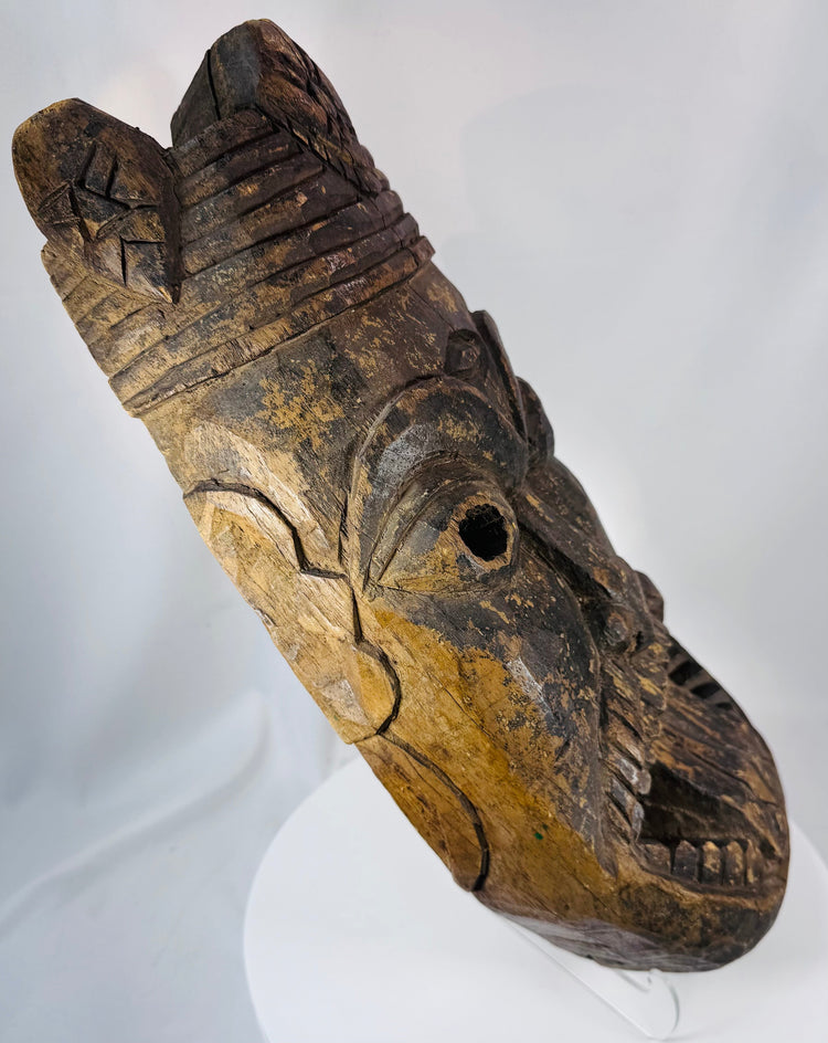 Ethnographic West African hardwood mask displaying bold spiritual imagery and weathered surface pigmentation.