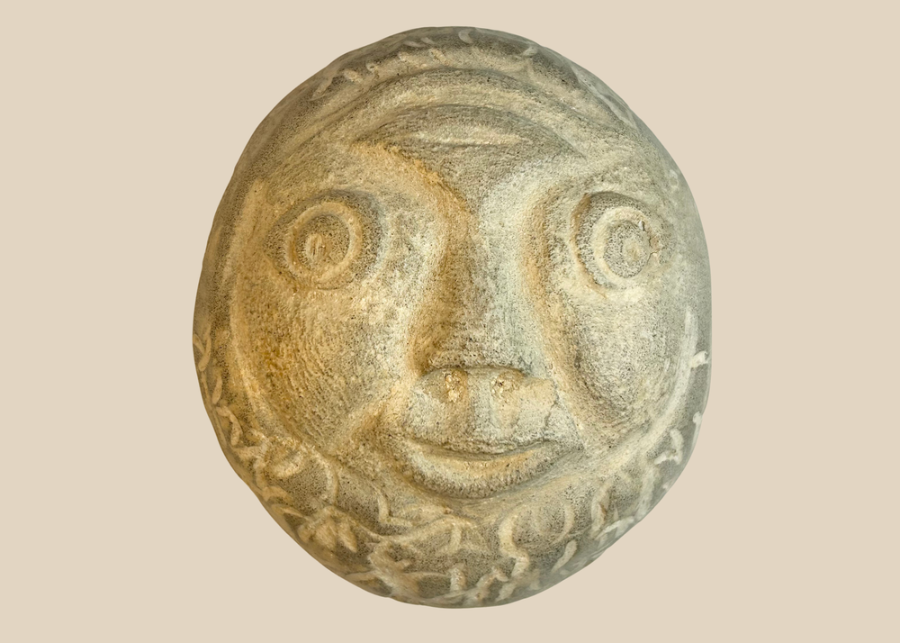 Hand-carved folk art stone face sculpture with expressive eyes and smiling mouth