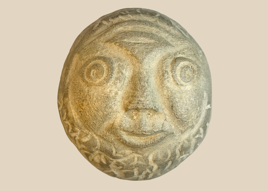 Hand-carved folk art stone face sculpture with expressive eyes and smiling mouth