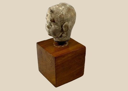 Small terracotta head fragment of a youthful male from the Hellenistic or early Roman period, with delicate features, subtle smile, and natural patina, mounted on a wooden display base.