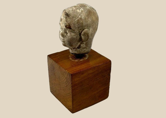 Small terracotta head fragment of a youthful male from the Hellenistic or early Roman period, with delicate features, subtle smile, and natural patina, mounted on a wooden display base.