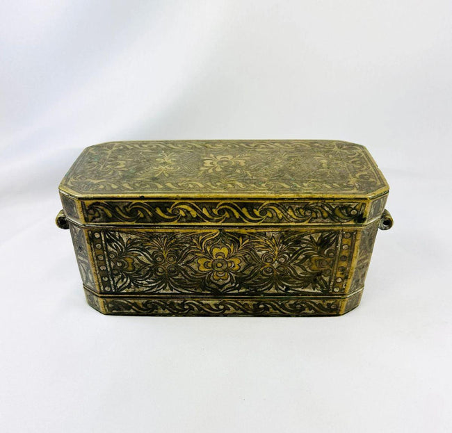 Antique rectangular betel nut box from Mindanao, Philippines, circa 1780–1820. Mixed metal alloy with brass and copper inlay featuring hand-engraved floral motifs, four internal hinged compartments, and side rings for suspension. Reflects Southeast Asian metalworking traditions and ceremonial betel chewing practices.