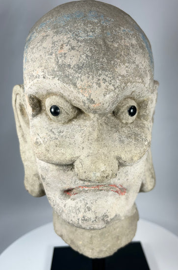 Early Chinese Buddhist stone sculpture fragment depicting a Luohan with traces of pigment.