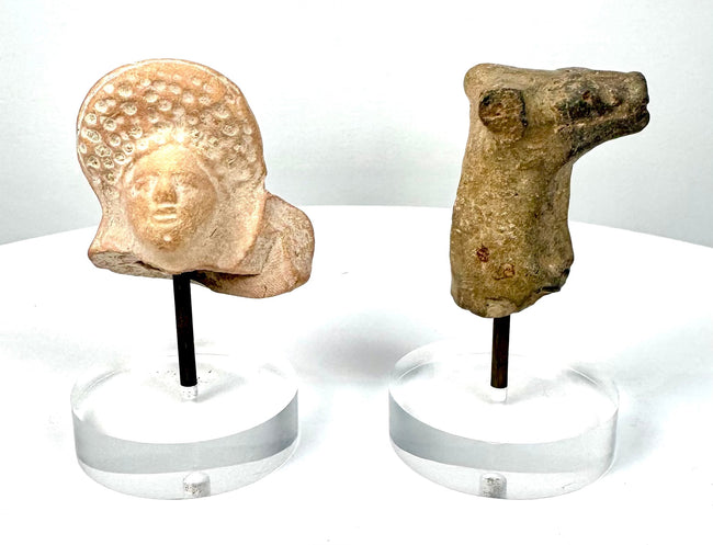 Pair of ancient terracotta fragments featuring a Roman Imperial female head and Mesopotamian animal sculpture on separate display stands.
