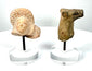 Pair of ancient terracotta fragments featuring a Roman Imperial female head and Mesopotamian animal sculpture on separate display stands.