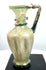 Late Roman glass jug with an elegant ovoid body, flared trumpet-shaped mouth, curved handle, and extensive ancient surface patination.