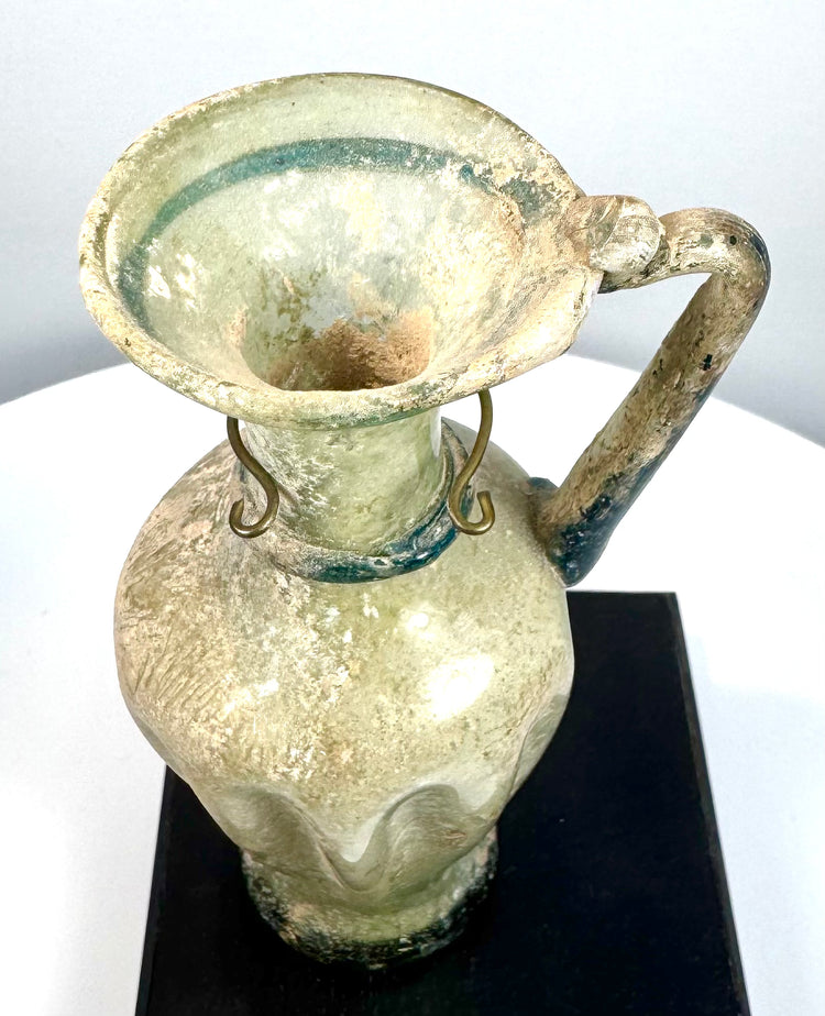 Ancient Byzantine blown glass vessel displaying an elongated neck, rounded rim, vertical body ribbing, and pale green glass construction.