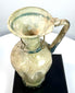 Ancient Byzantine blown glass vessel displaying an elongated neck, rounded rim, vertical body ribbing, and pale green glass construction.