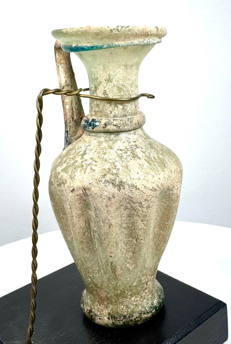 Ancient Roman pale green glass vessel featuring pronounced vertical ribbing, a slender cylindrical neck, and applied blue-green decorative trails.