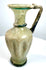 Ancient Eastern Mediterranean glass jug displaying textured vertical ribs, blue-green decorative glass threads, and natural surface deterioration.