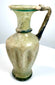 Ancient Eastern Mediterranean glass jug displaying textured vertical ribs, blue-green decorative glass threads, and natural surface deterioration.