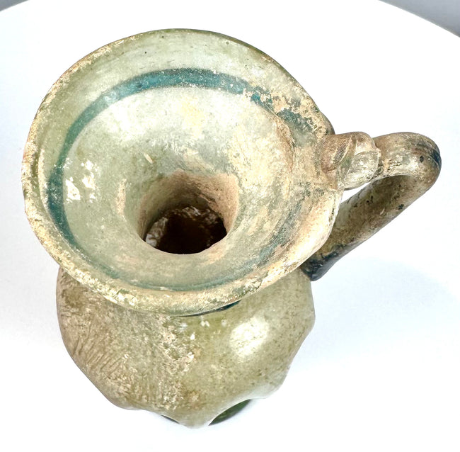 Late Roman blown glass jug with a trumpet-shaped opening, curved shoulder-to-rim handle, and surviving ancient decorative glasswork.
