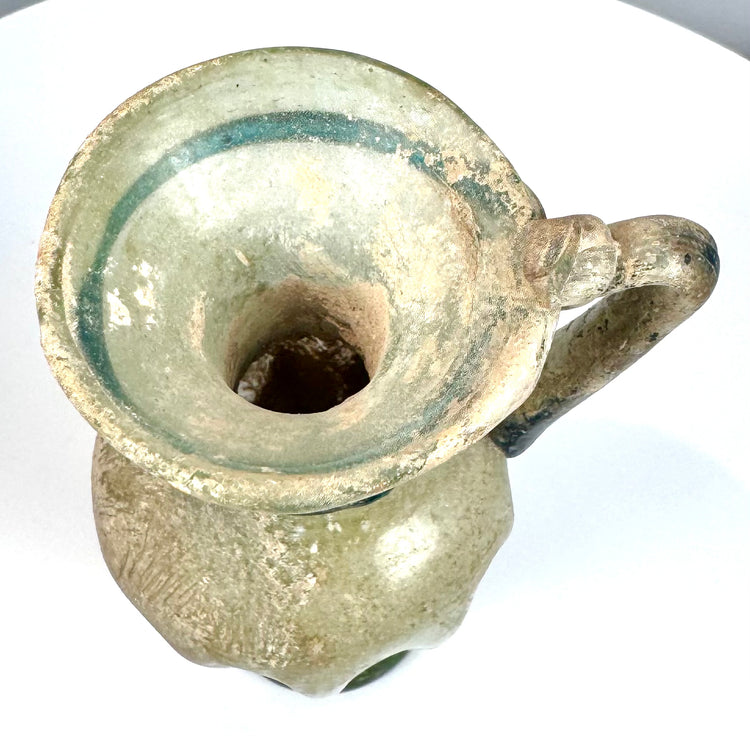 Late Roman blown glass jug with a trumpet-shaped opening, curved shoulder-to-rim handle, and surviving ancient decorative glasswork.