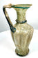 Ancient Roman ribbed glass jug exhibiting traditional pulled glass handle construction and applied decorative elements from the 4th–5th century CE.