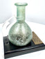 Roman Imperial glass perfume bottle with a long cylindrical neck, rounded body, and historical identification plaque referencing the Land of Israel.