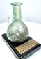 Ancient Roman free-blown glass vessel exhibiting pale turquoise coloration, earthy encrustations, and traditional early Imperial glassmaking characteristics.