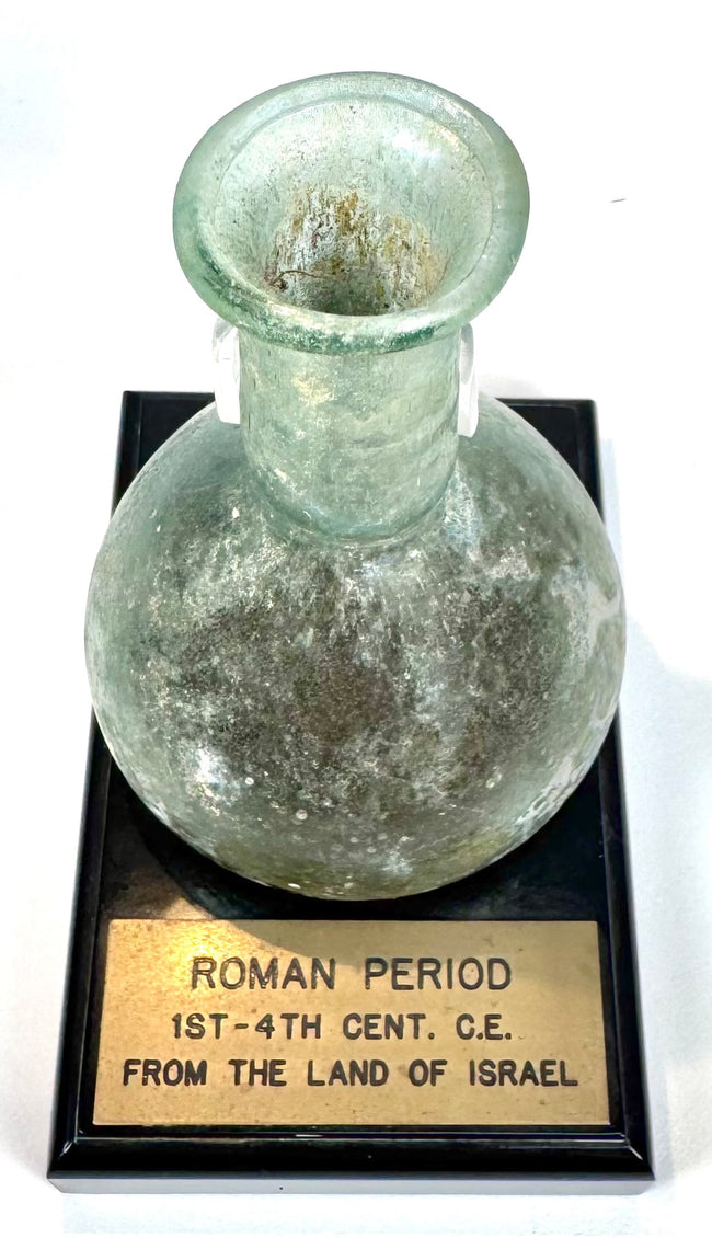 Roman glass unguentarium from the 1st–2nd century CE, displaying a globular body, folded rim, and extensive archaeological surface weathering.