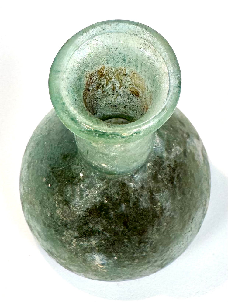 Early Roman sea-green glass unguentarium displaying a spherical body, thickened flaring rim, and weathered glass surface with iridescent deposits.