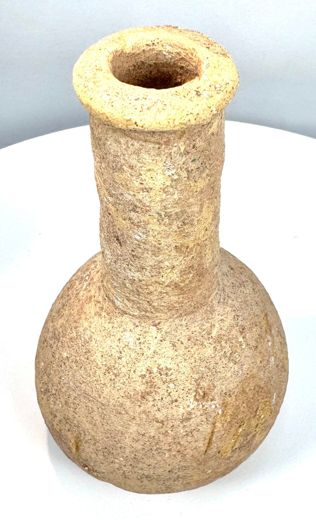 Ancient Roman stone unguentarium featuring a thickened circular lip, narrow opening, and visible weathering along its elongated neck.