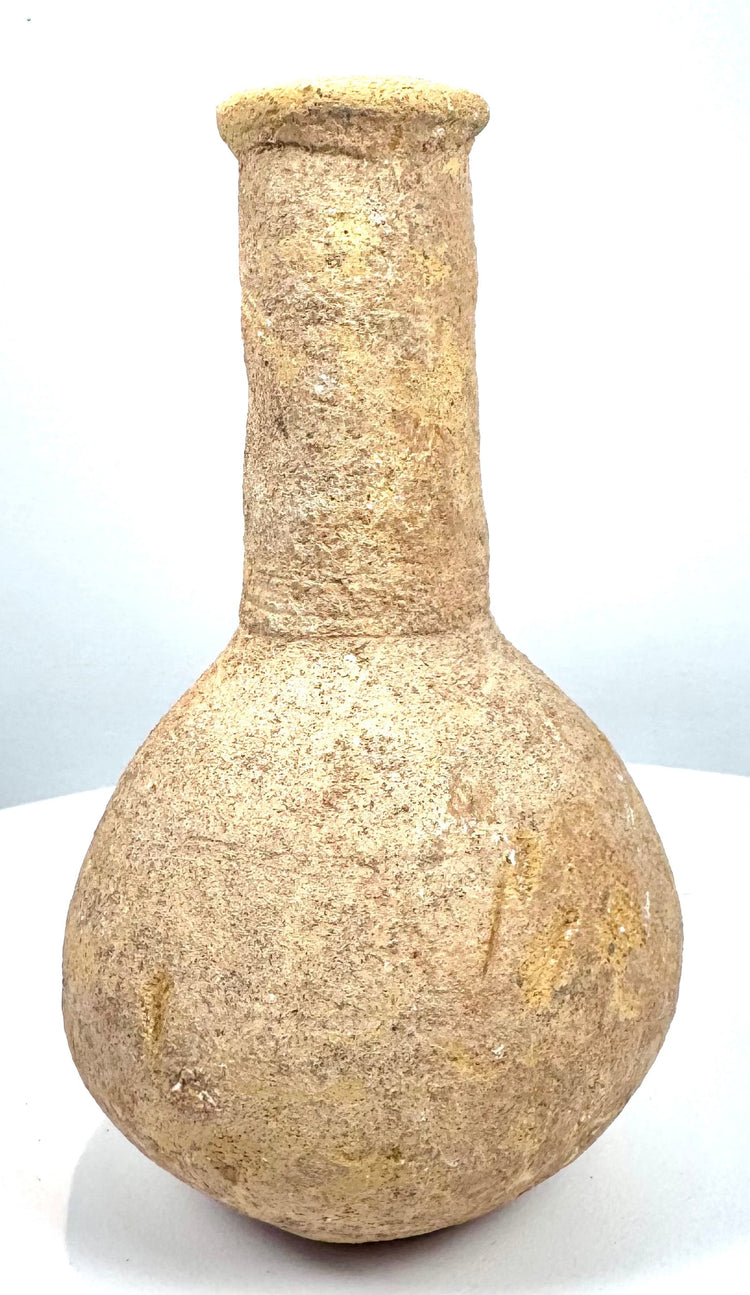 Roman Imperial perfume container with a nearly spherical body, pale buff-coloured stone surface, and scattered earthy encrustations.