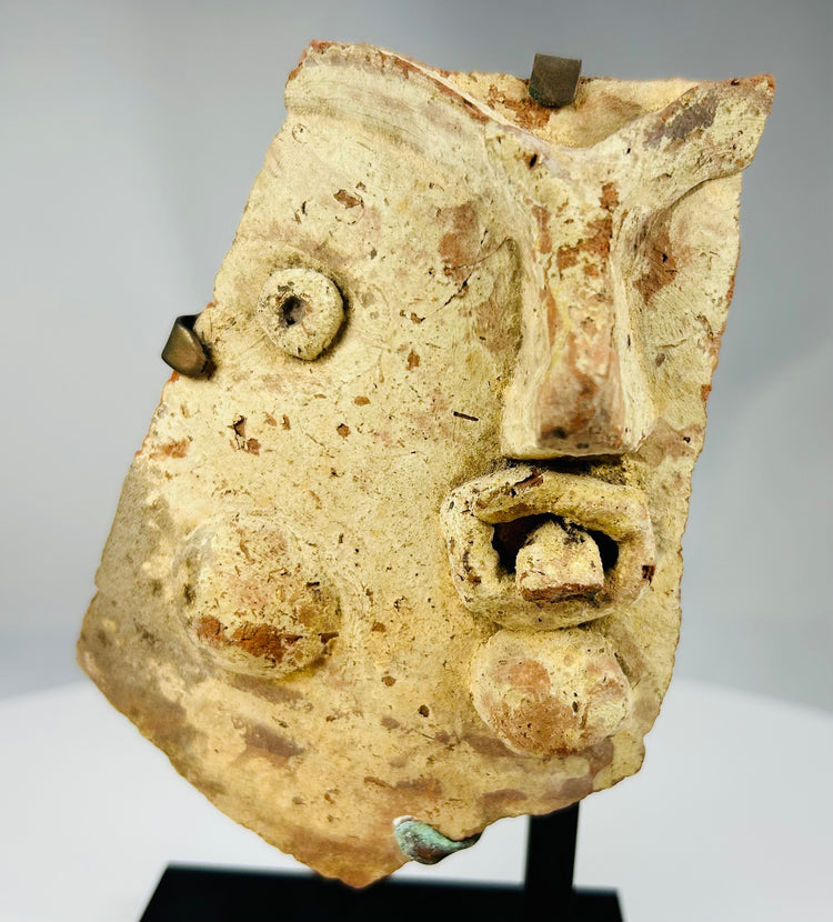 Ancient Mediterranean theatrical artifact fragment featuring stylized mask facial details in fired clay.