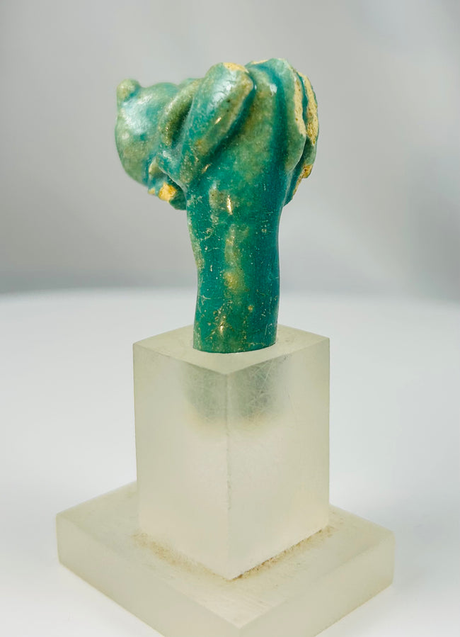 Ancient Egyptian faience cat head fragment symbolizing Bastet mounted on display stand.