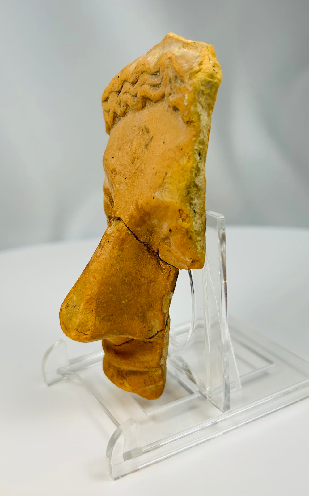 Ancient terracotta theatre mask fragment with stylized wavy hair and prominent nose