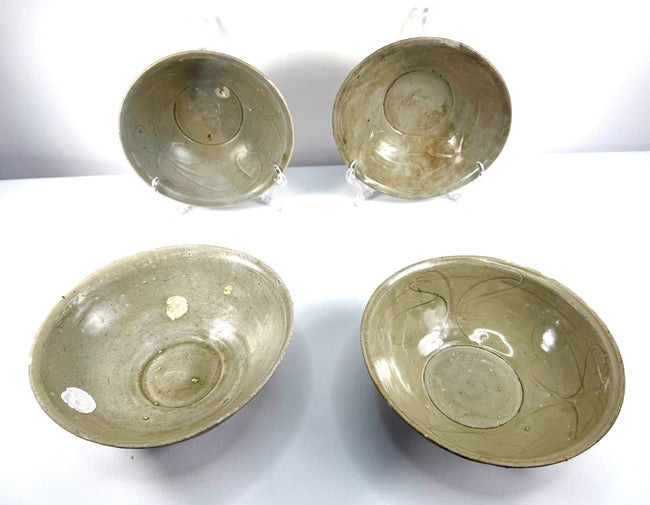 Four Song Dynasty Chinese ceramic bowls featuring pale green celadon glaze, incised floral decorations, and marine encrustations from centuries of underwater submersion.
